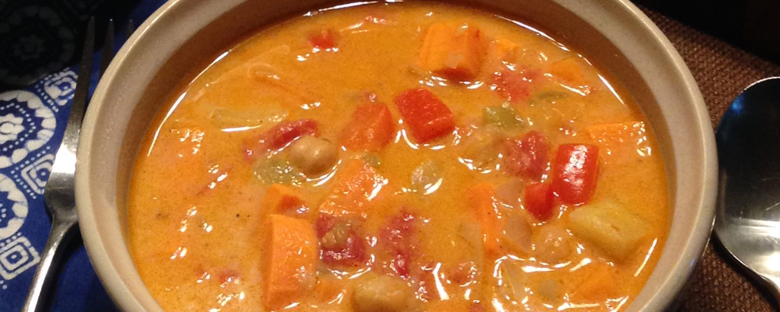 A bowl of Moroccan Coconut Chickpea Soup artfully displayed on a tabl with bread and a salade